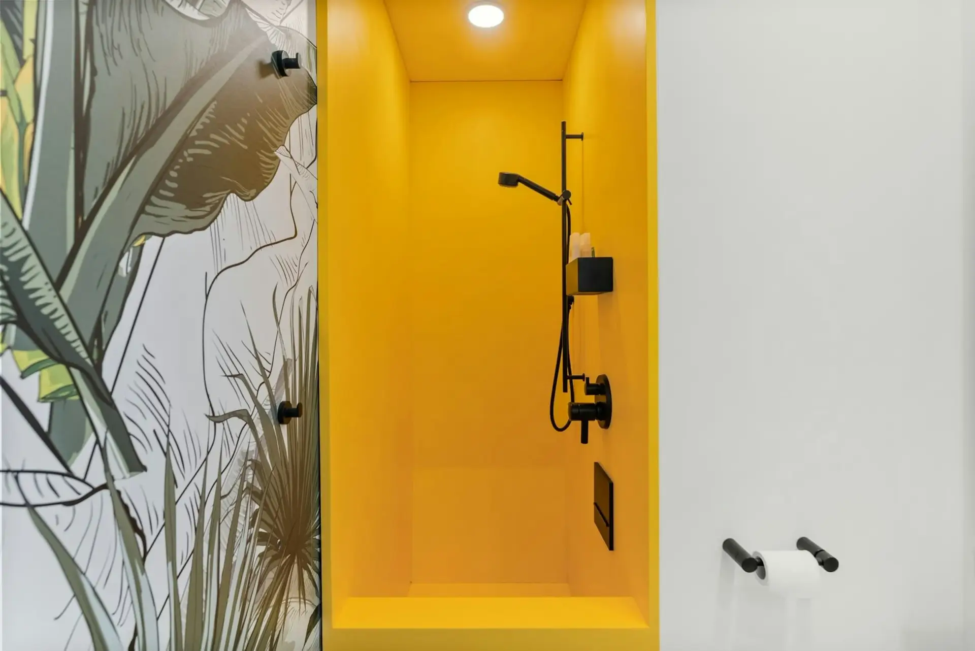 Modern bathroom renovation with a bright yellow walk-in shower, black fixtures and tropical wallpaper