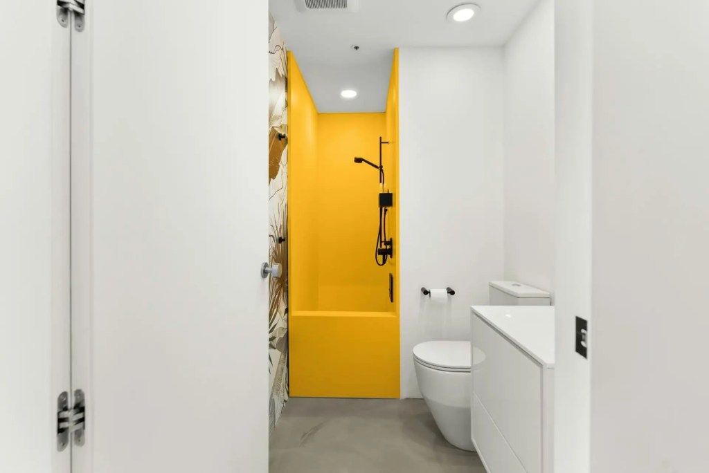 Modern narrow bathroom renovation with a bright yellow walk-in shower, black fixtures and white vanity