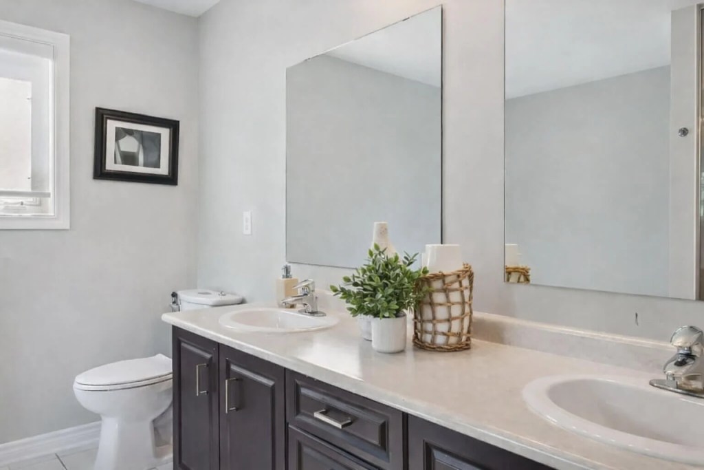 Bathroom renovation in Oshawa, Ontario featuring a modern double vanity with dark wood cabinets, stone countertop, and frameless mirrors